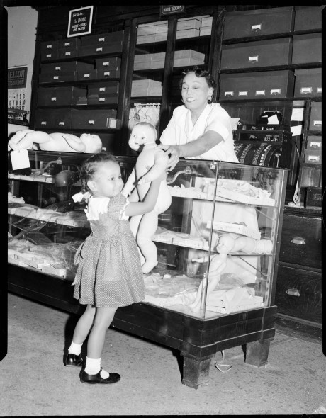 Girl Lifting Up Naked Baby Doll Without Head Over Counter To Woman Standing On Other Side In Stevenson Doll Cmoa